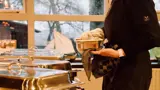 Een medewerker bereidt het buffet voor, met een van de voedselcontainers in de hand.